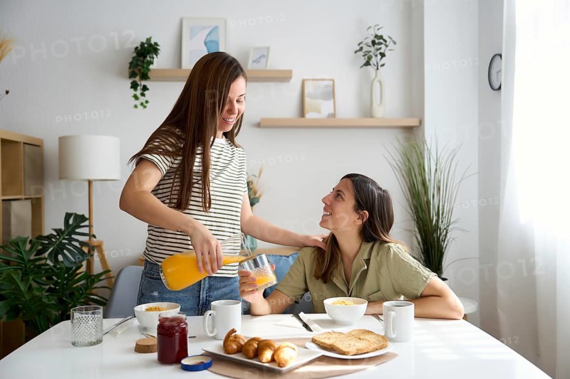 A lesbian couple shares a warm, intimate breakfast at home Natural light fills the room, highlighting their joyful expressions and the bond they share