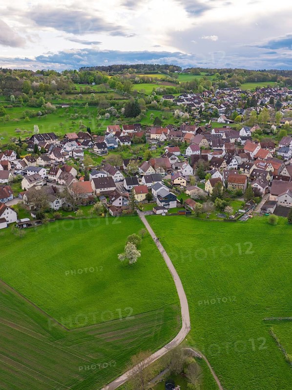 A winding footpath leads across a large green meadow to a village, Ostelsheim, district of Calw, Germany
