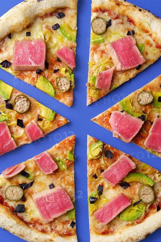 Top view image of a pizza sliced into eighths, topped with seared tuna, avocado, leek, cilantro, and a creamy tomato sauce on a baked crust