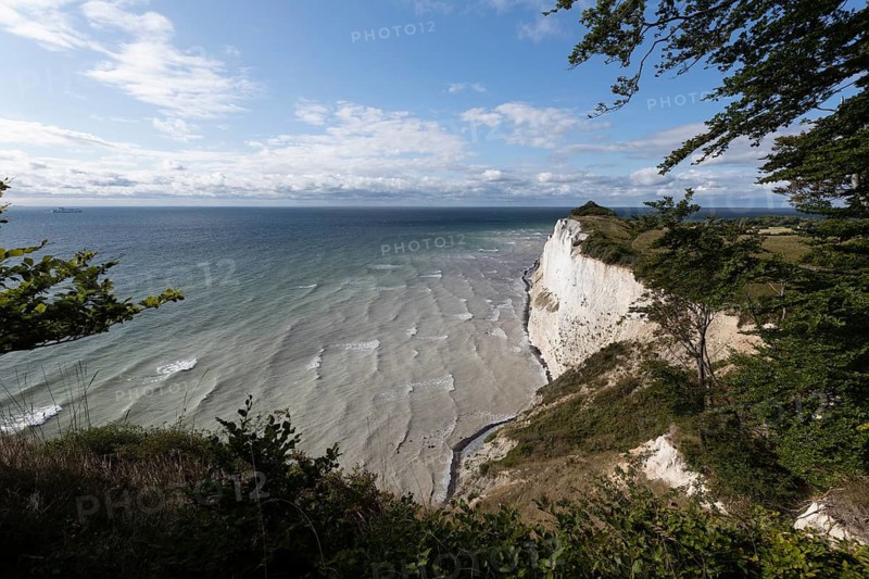 White chalk cliffs at Hundevængsfald with a view of the Baltic Sea towards Møn Lighthouse under a clear blue sky. Møns Klint, Region Sjælland, Denmark