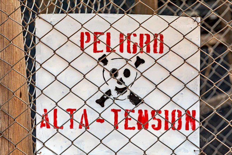 Spanish warning sign with skull and lettering 'Peligro Alta Tension' behind a chain link fence, danger sign on the silver mines near Potosi on Cerro Rico in Bolivia