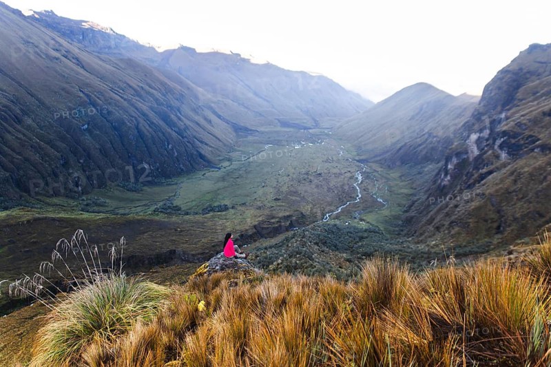 Ecuadorian woman in pink jacket peacefully gazes over the expansive, lush valley from El Altar volcano, Ecuador, capturing the serene beauty and grandeur of nature