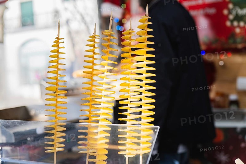 Close-up of spiral tornado potatoes on sticks displayed at an outdoor market. The vibrant yellow twists create a visually appealing snack presentation