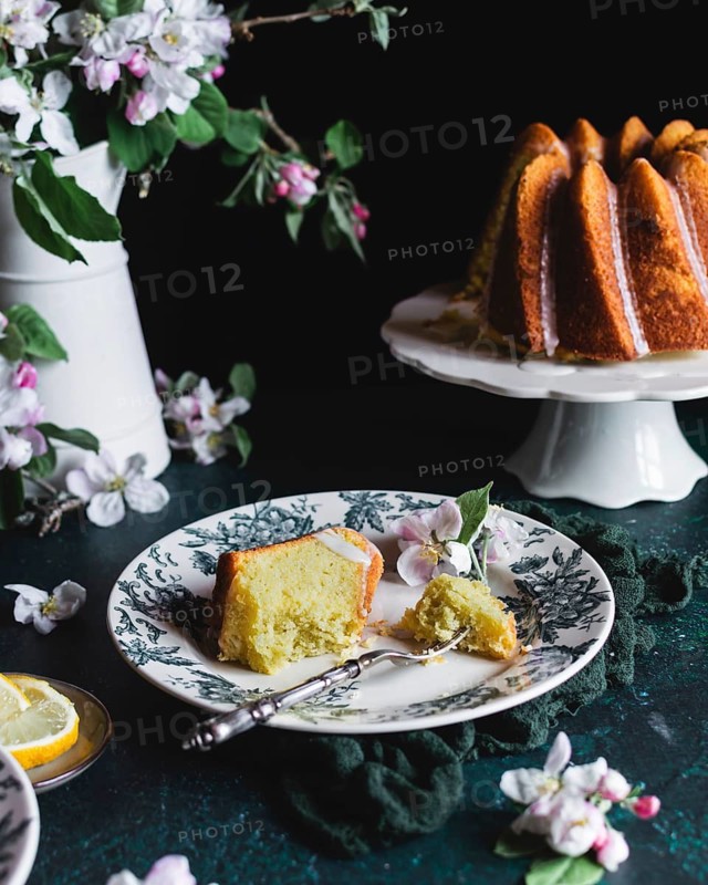 A delectable spring lemon bundt cake served on a decorative plate, complemented by vibrant blossoms and sliced lemons, creating a refreshing and elegant dessert presentation