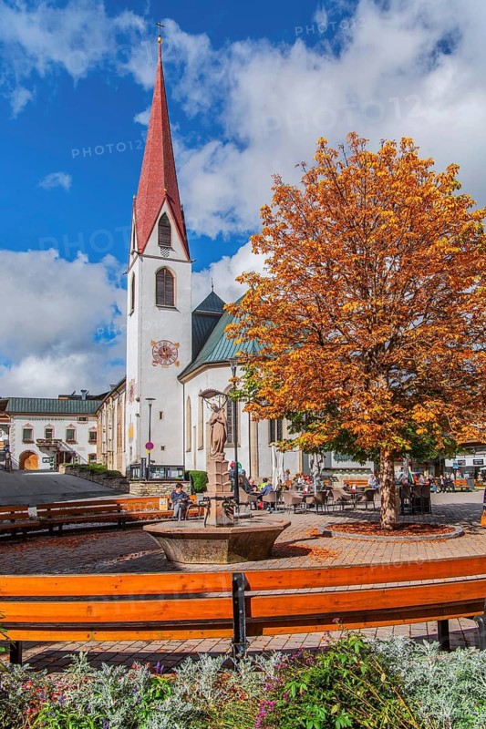 Fountain on the village square with the pilgrimage church of St. Oswald in autumn, Seefeld in Tyrol, Seefeld Plateau, Tyrol, Austria