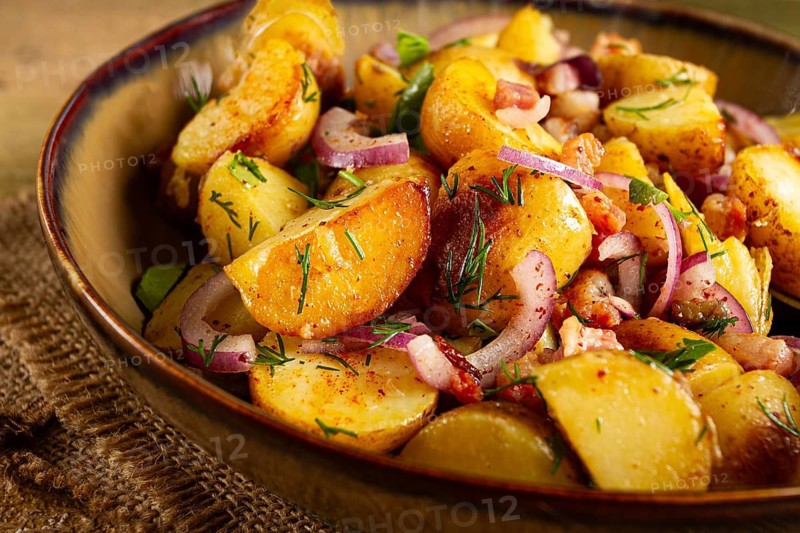 German potato salad with bacon, onions and herbs, plate on a wooden table, rustic style, no people