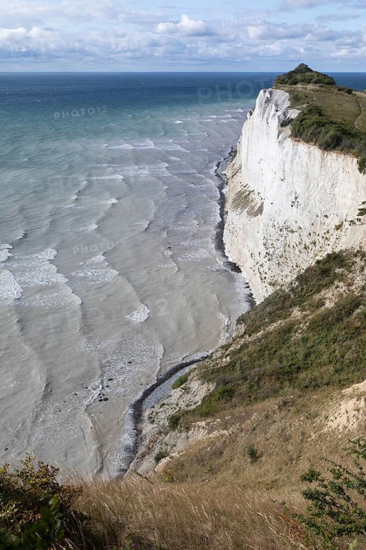 White chalk cliffs at Hundevængsfald with a view of the Baltic Sea towards Møn Lighthouse under a clear blue sky. Møns Klint, Region Sjælland, Denmark