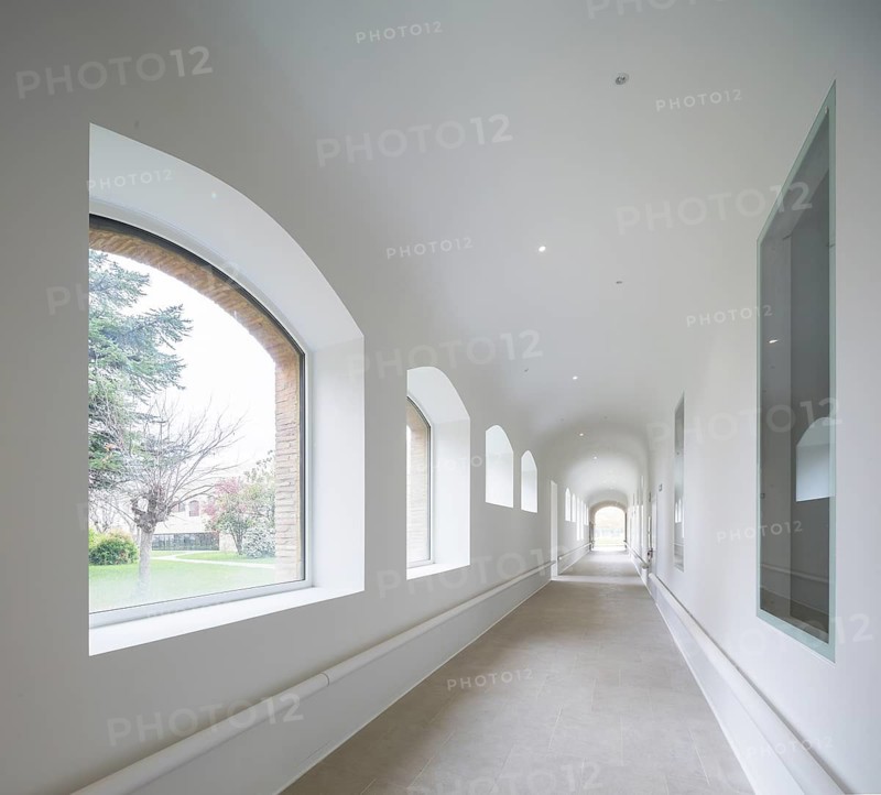 A luminous corridor of hospital featuring large arched windows, allowing ample natural light. The minimalist style with neutral tones creates a serene and elegant atmosphere