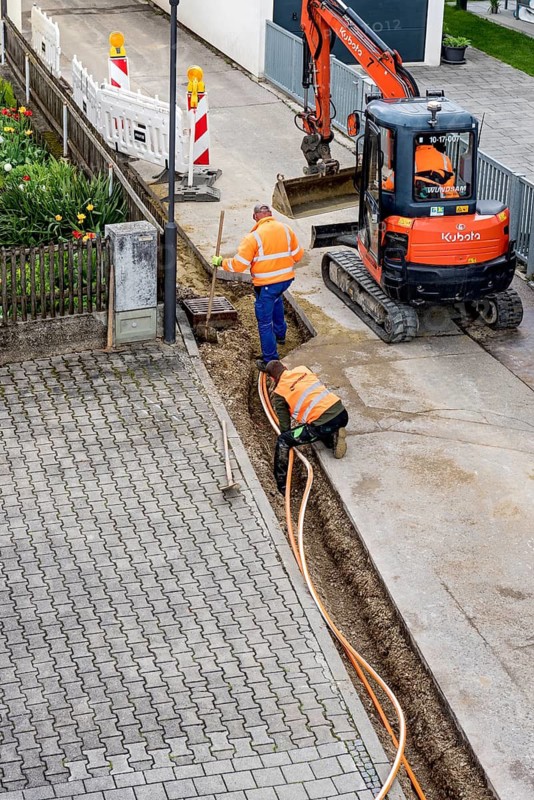 Construction workers lay fibre optic cable in trench under asphalt, cable trench, excavator, construction site, fibre optic expansion, fast Internet, residential area, rural, village, Marzling, Upper Bavaria, Bavaria, Germany