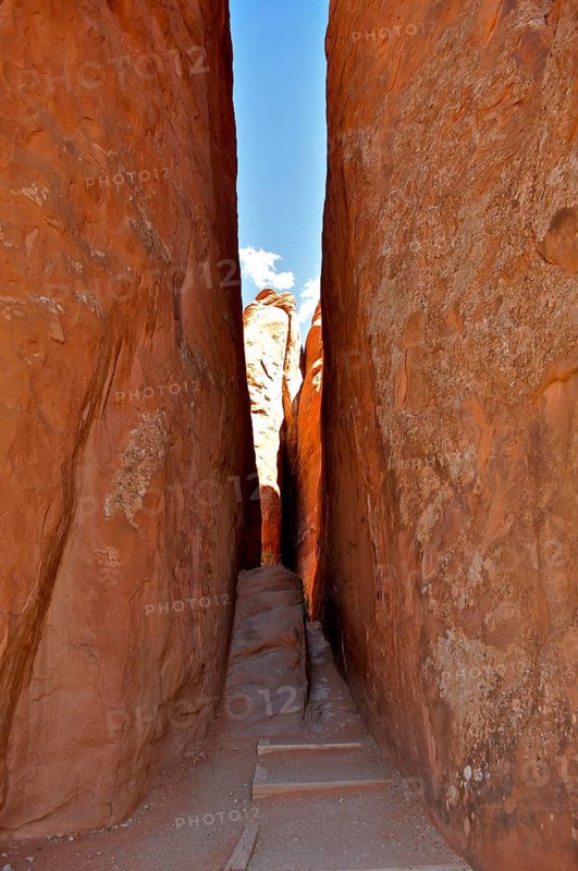 A narrow passage of a hiking trail between high sandstone walls, into which light is just falling, Arches National Park, Utah, USA