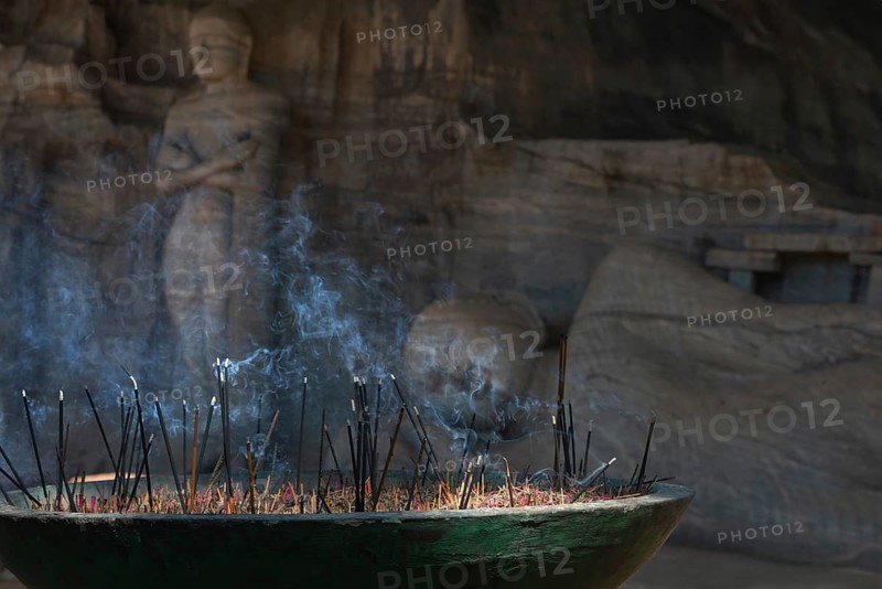 A serene scene of incense sticks burning with smoke rising in front of an ancient stone Buddha statue in a Sri Lankan temple, capturing tranquility and spirituality
