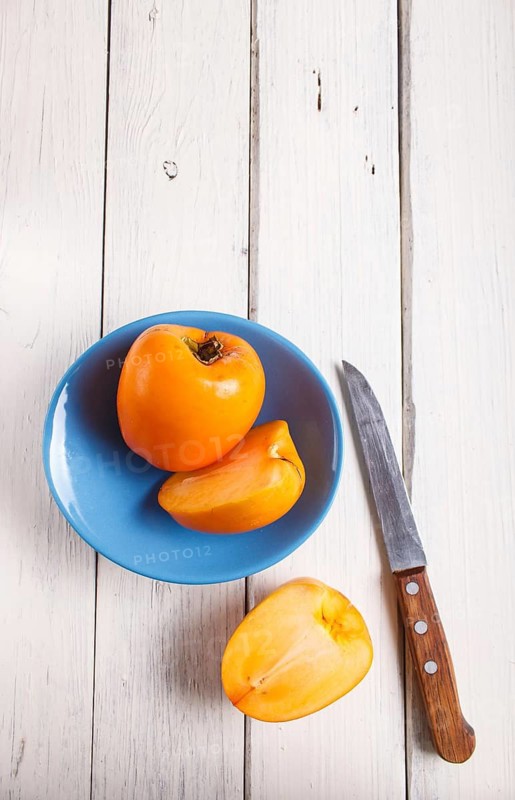 Ripe orange persimmon in a blue plate on white wooden background, with copy space