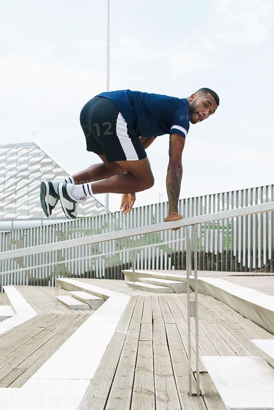 A black male athlete demonstrates agility and strength as he trains outdoors, showcasing dynamic movement and focus. Ideal for fitness, sports, and lifestyle themes