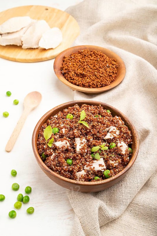 Quinoa porridge with green pea and chicken in wooden bowl on a white wooden background and linen textile. Side view, close up