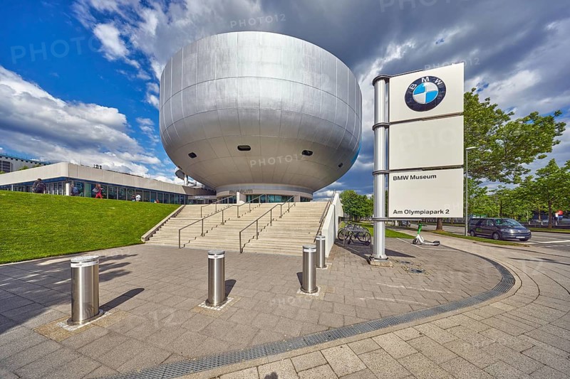 Car museum, BMW museum, commercial building, modern architecture, barrier bollard, concrete staircase, metal railing, sidewalk, meadow, trees, blue sky, white and dark gray cumulus clouds, Am Olympiapark, Georg-Brauchle-Ring, Lerchenauer Straße and Petuelring intersection, Munich, state capital, district-free city, Bavaria, Germany