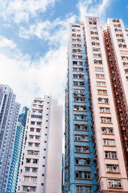 Tall residential buildings dominate the Hong Kong cityscape, showcasing vibrant architecture and urban density against a backdrop of clear blue sky and scattered clouds