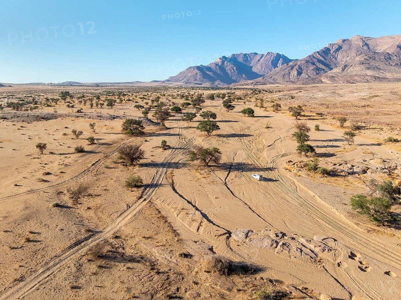 Aerial view of off-road car driving in dry riverbed and desert landscape on the Ugab River, behind Brandberg, Erongo, Damaraland, Namibia