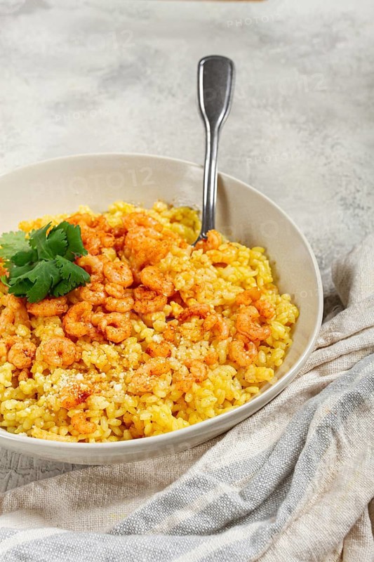 Risotto with shrimp, in a bowl, on a textured surface, with a side dish of fresh coriander, homemade, no people