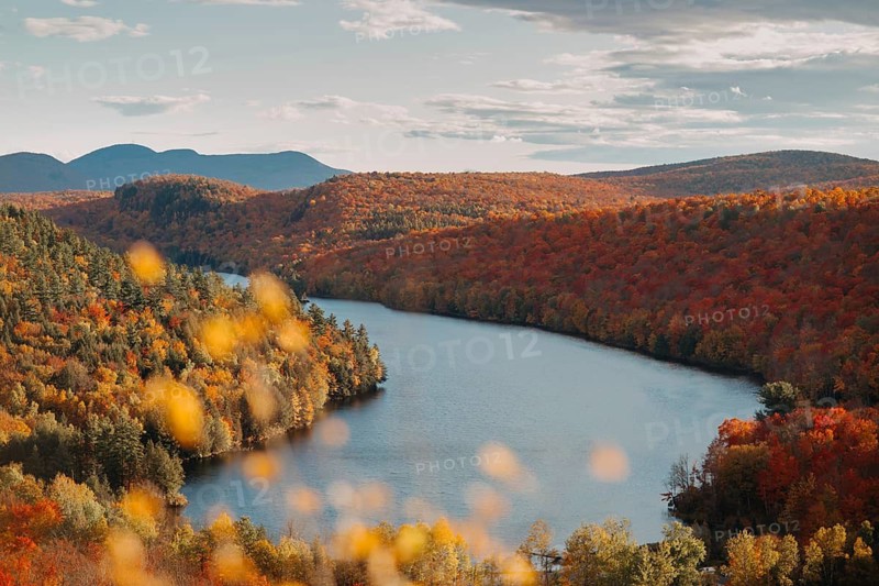 A breathtaking view of Quebec's countryside during autumn, showcasing a river winding through vibrant foliage with a backdrop of rolling hills and a partly cloudy sky