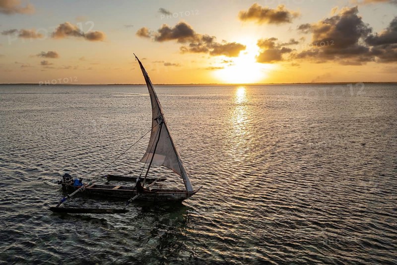 Traditional sailboat against a serene, golden sunset on calm water