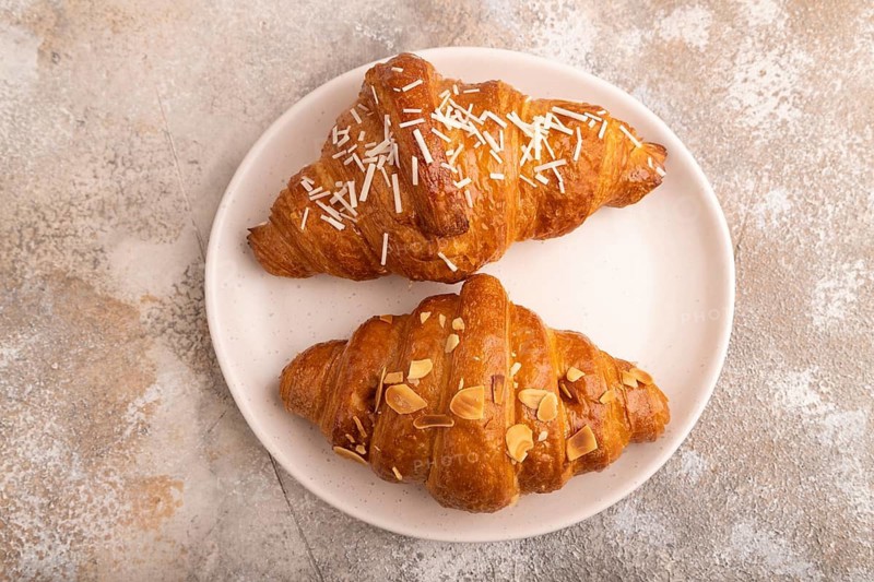 Croissant on white plate on brown concrete background, top view, flat lay, close up
