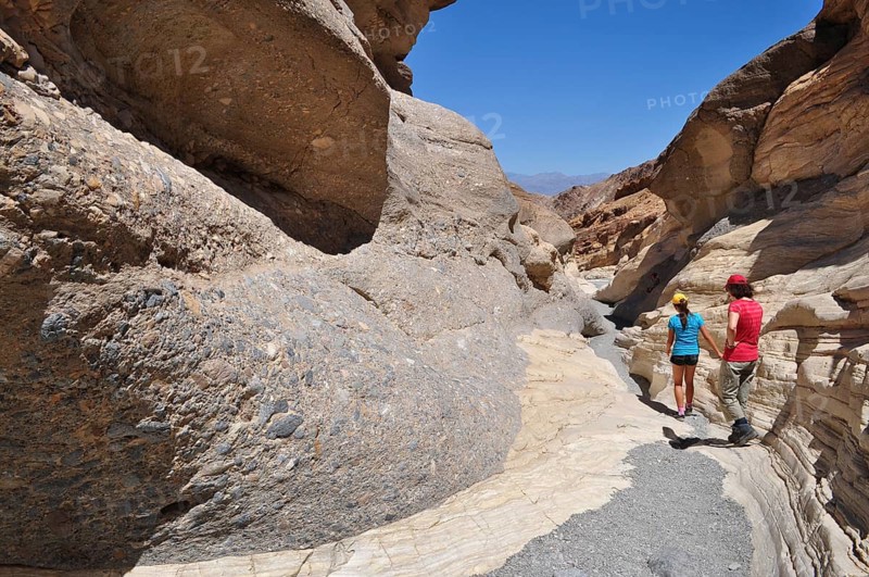 Two people hiking through a sunny gorge with large rock formations, Death Valley National Park, Mojave Desert, California, Nevada, USA