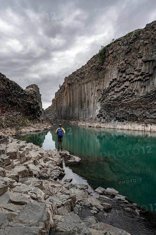 Tourist standing by the river in Stuðlagil Canyon, turquoise blue river between basalt columns, Egilsstadir, Iceland