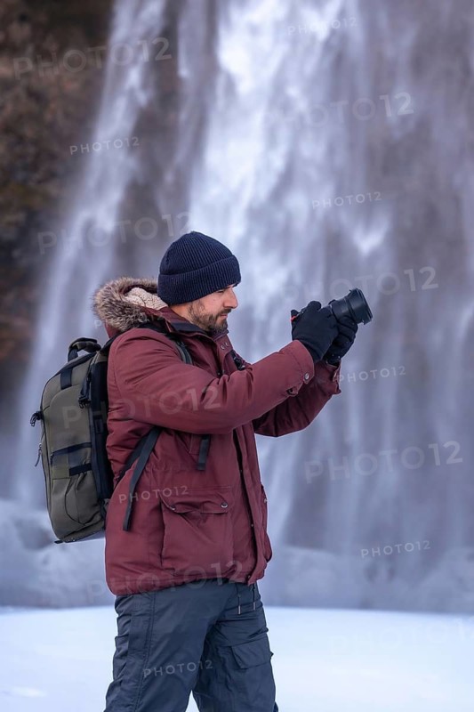 A photographer taking pictures in winter at the Seljalandsfoss waterfall with snow in Iceland