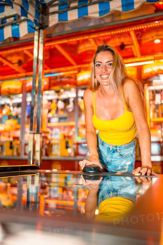 Vertical photo of a happy woman playing air hockey and having fun in an amusement arcade