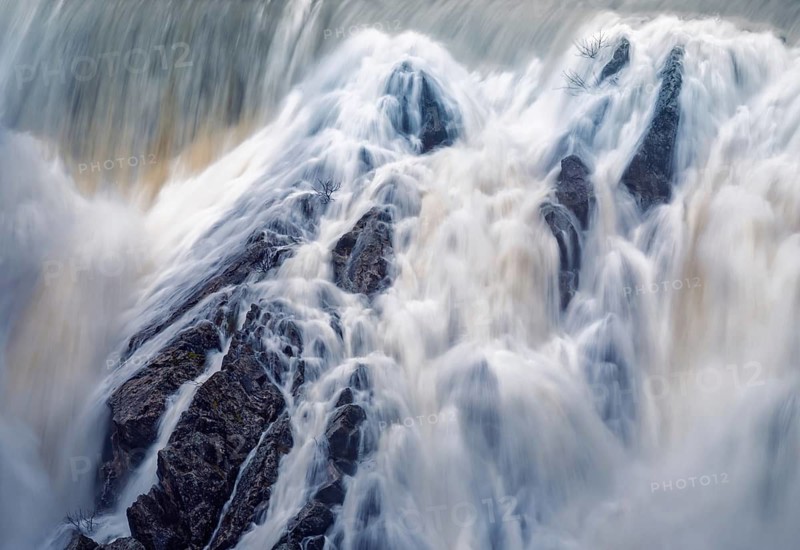 Captivating long exposure shot of cascading water over rugged rocks at Presa del Villar reservoir near Madrid, illustrating the dynamic movement and serene nature of the water
