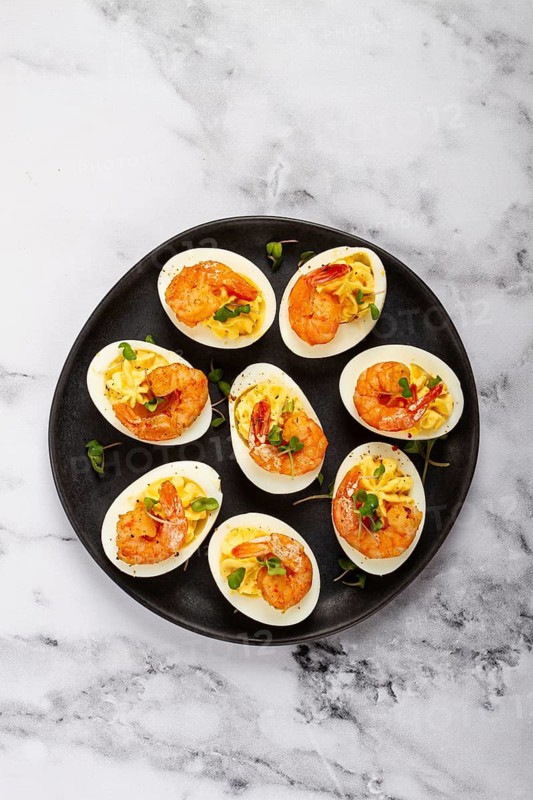 Boiled eggs stuffed with yolk and seasoned with mayonnaise, stuffed eggs with shrimp, on a black plate, selective focus, close-up, no people