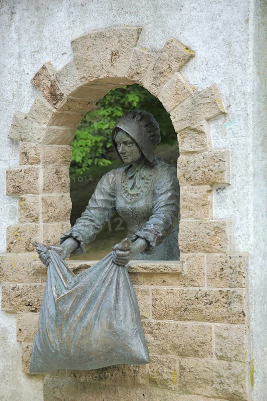 Monument to Brothers Grimm fairy tale Frau Holle, figure, cushion, window, shake, fairy tale figure, sculpture, Brothers Grimm, looking out, look, Frau Holle Park, Hessisch Lichtenau, Hesse, Germany
