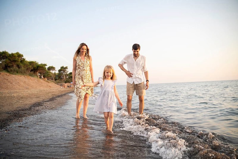 A cheerful family walks along an Italian beach as the sun sets, enjoying the waves and the warm atmosphere. Perfect moment of relaxation and togetherness by the sea