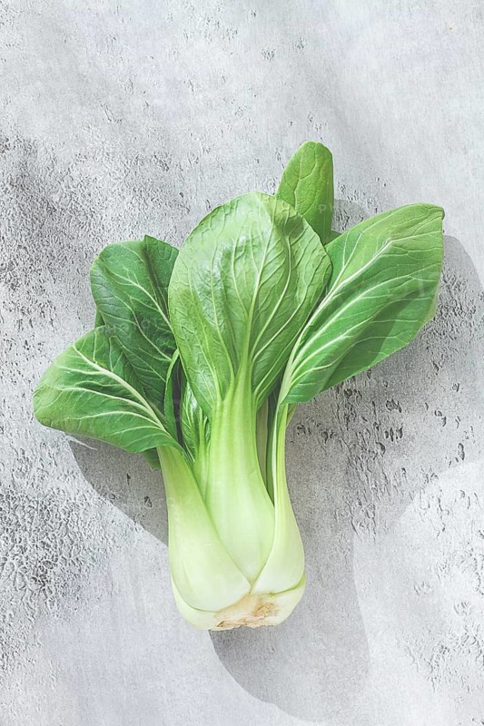 Fresh bok choy, laid out on a light gray surface, top view, natural light