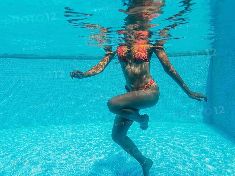 A woman in a colorful bikini is gracefully floating in a clear blue pool. Sunlight dances on the water's surface, creating a serene, tranquil atmosphere
