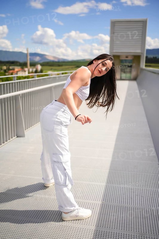 Vertical photo of a caucasian young woman dancing urban choreography on a bridge