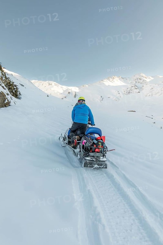 A man rides a snowmobile up a snow-covered mountain, surrounded by a breathtaking winter landscape under a clear blue sky. Perfect for winter sports enthusiasts