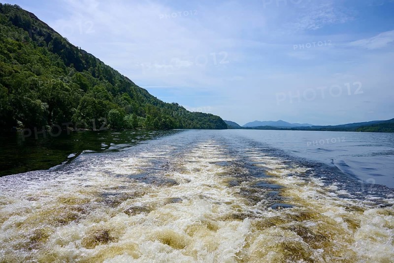 A river with waves from a boat surrounded by green hills and a blue sky, Fort Augustus, Loch Ness, Scotland, United Kingdom, United Kingdom
