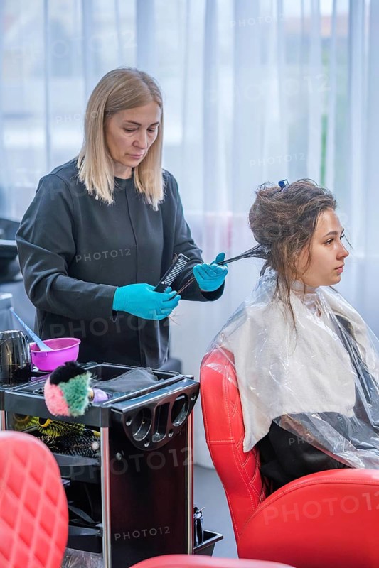 A hair stylist applies keratin treatment to a woman's hair in a beauty salon. The process is part of a hair straightening procedure to help smooth the hair texture