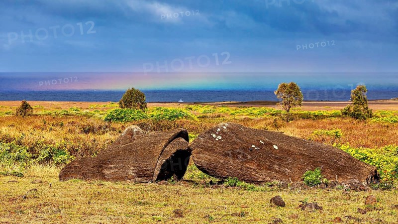 Boulders in a dry meadow with rainbows over the sea, The Moai statues on Easter Island in the Pacific Ocean
