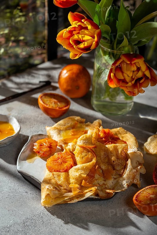 Light and airy crepes Suzette topped with a rich sauce made from caramelized sugar, butter, and fresh blood orange juice, accompanied by vivid tulips and fresh blood oranges