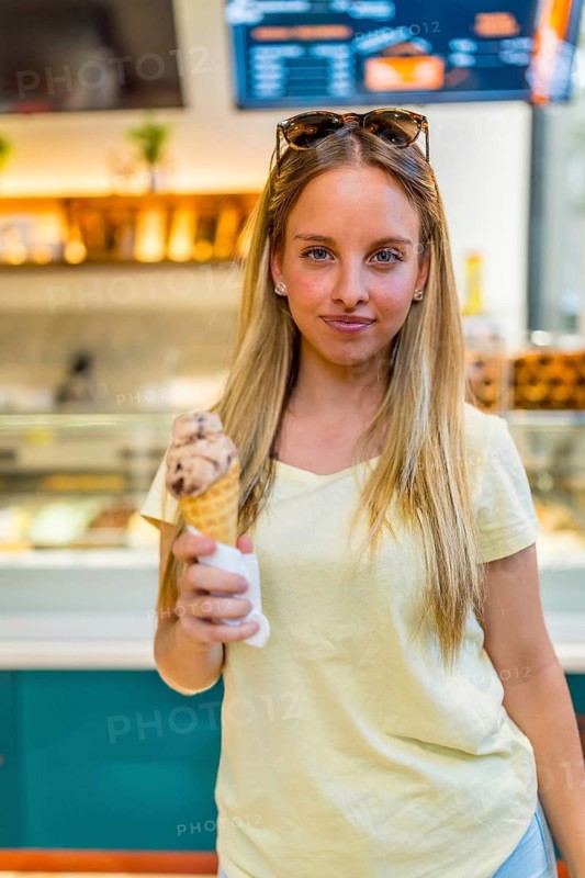 Vertical portrait of a blonde chic woman eating ice cream cone in store