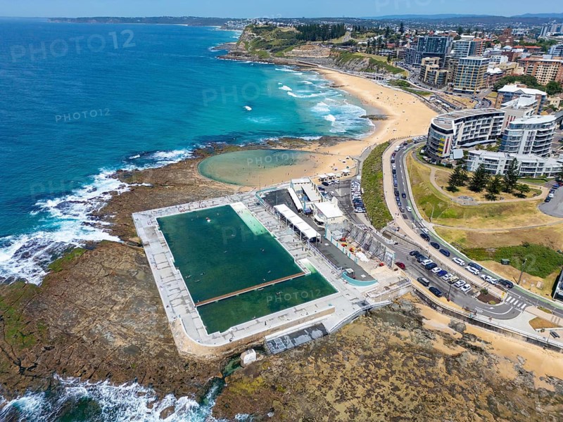 Aerial view of the stunning coastal landscape of Newcastle, New South Wales, Australia. It features an inviting ocean pool, sandy beaches, and nearby urban development