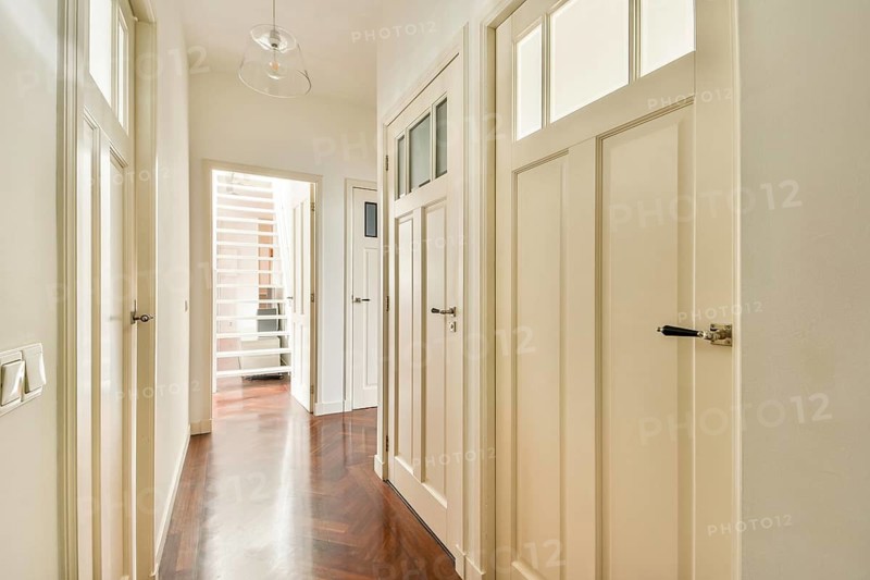 A well lit hallway featuring polished wooden flooring and several white panel doors, accented by a modern pendant light. The space exudes elegance and simplicity
