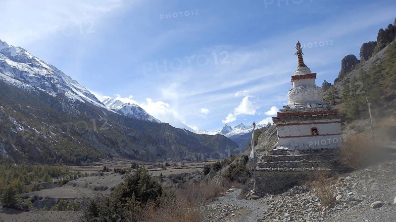 White stupa in front of a majestic mountain landscape with clear skies, trekking at Annapurna Circuit, Manang, Nepal