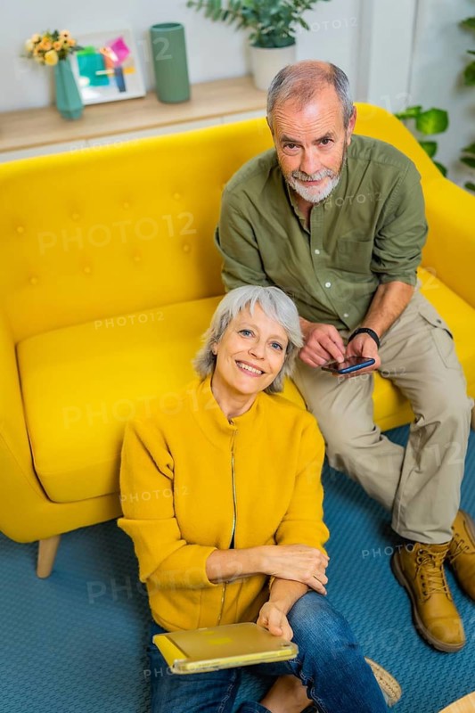 Vertical top view portrait of a senior couple relaxed at home together holding mobile phone and digital tablet
