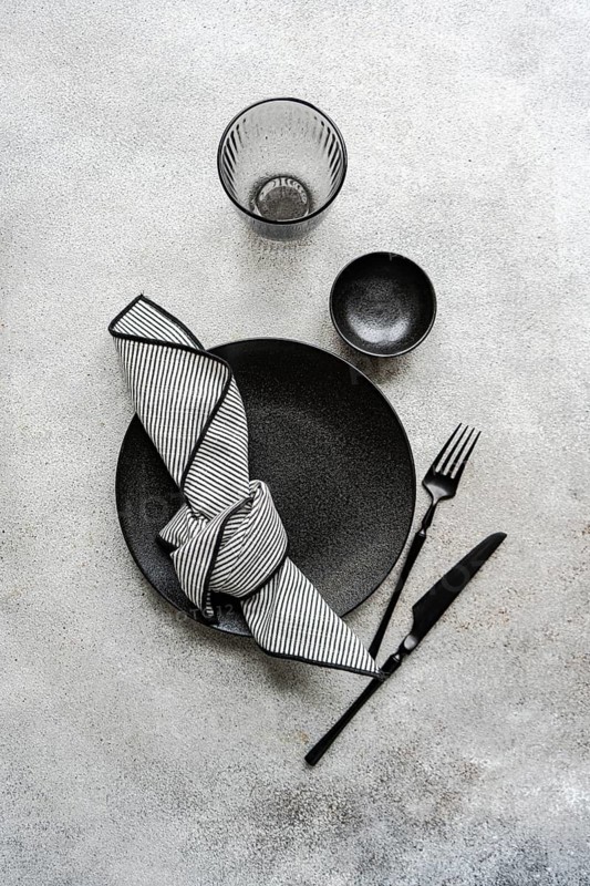 A sophisticated black and white table setting features a textured plate, stylish glassware, striped napkin, and sleek cutlery. Perfect for a modern dining ambiance