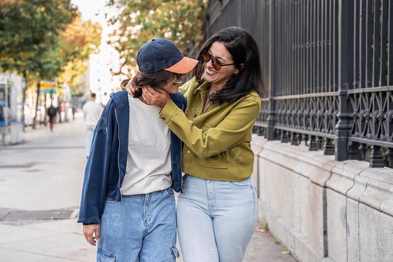 A joyful lesbian couple shares a loving moment while walking along a city street. They embrace, radiating happiness and connection, surrounded by vibrant autumn foliage