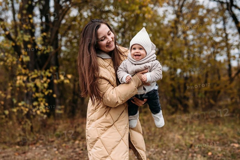 A cheerful mother holds her smiling baby during a peaceful autumn walk in the forest. They enjoy the crisp air and the golden hues, creating precious family memories