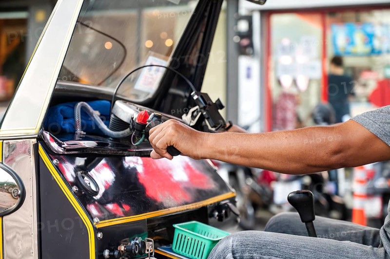 Cropped unrecognizable male Thai tuk tuk driver navigating a black vehicle through the bustling streets of Chiang Rai, Thailand